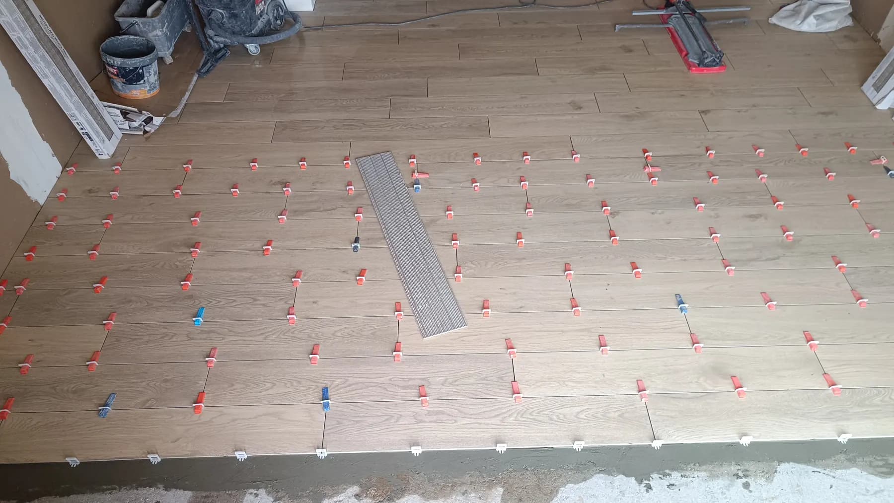 Light wood-effect plank tiles being laid with a levelling system